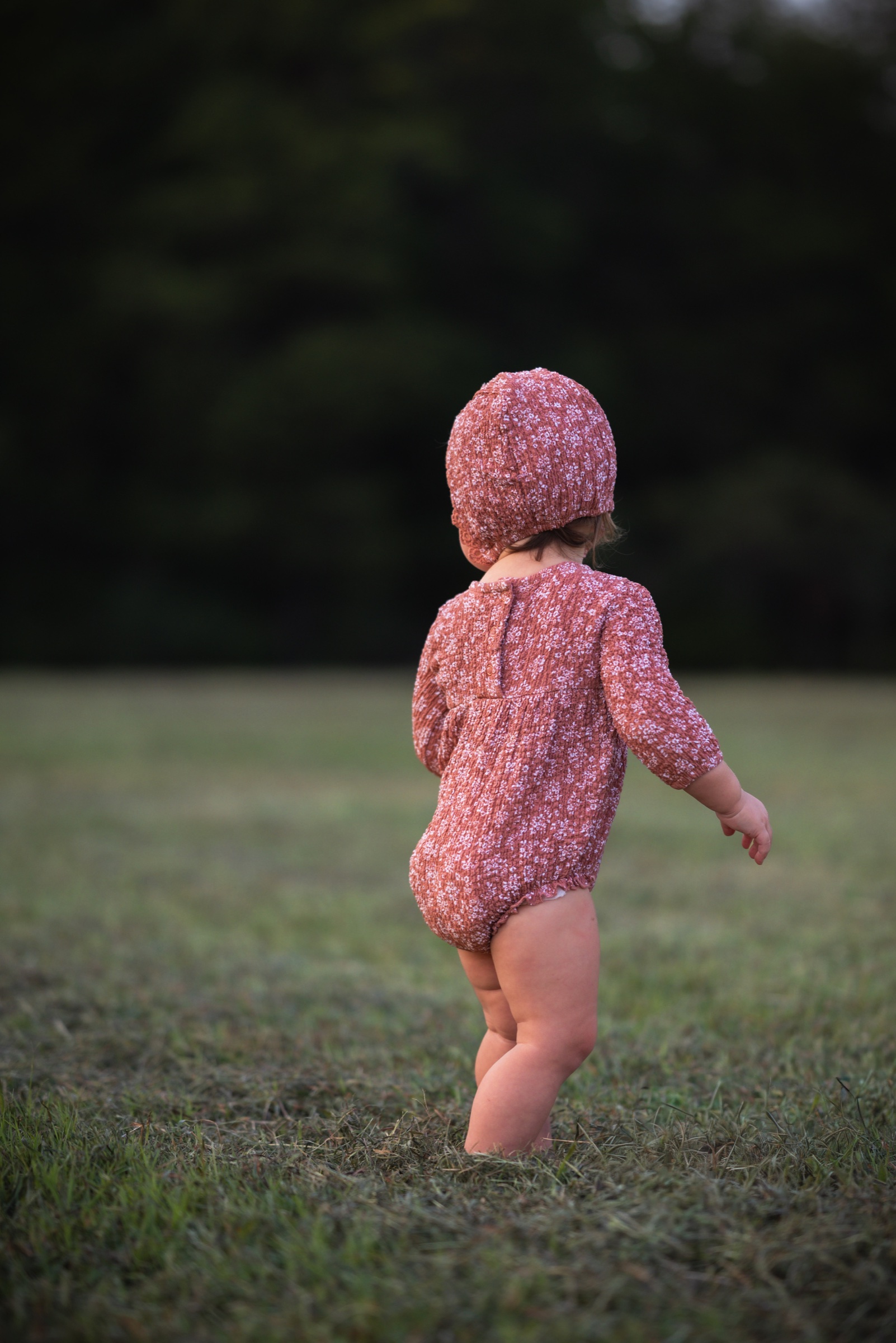 Young child exploring a grassy field in a rust-colored knit outfit