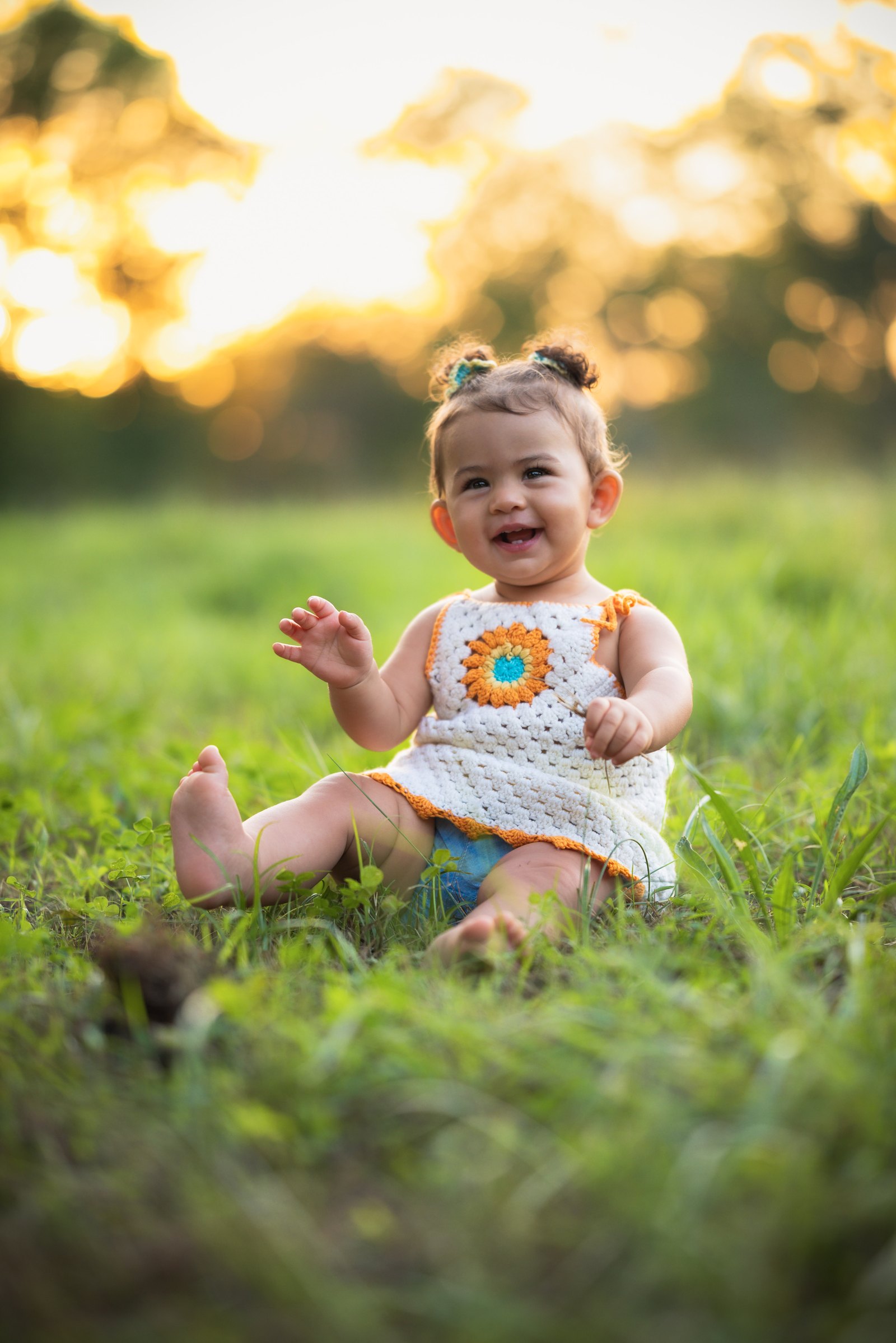 Smiling baby in a handmade sunflower top sitting in a glowing field