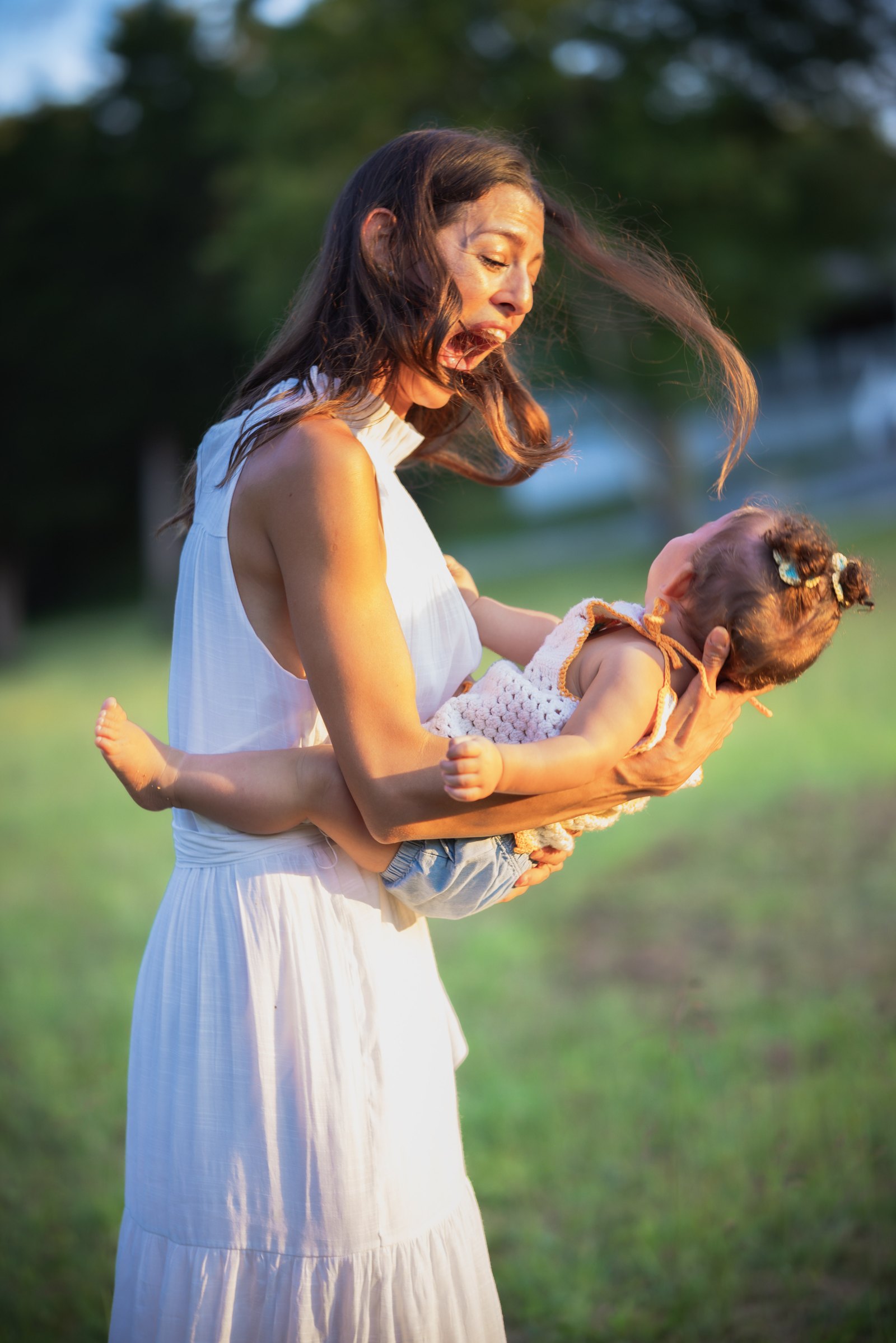 Mother laughing while playfully holding her baby in warm evening light