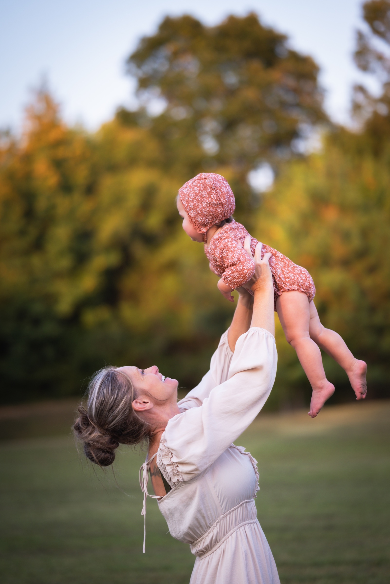 Mother joyfully lifting her baby into the autumn evening light