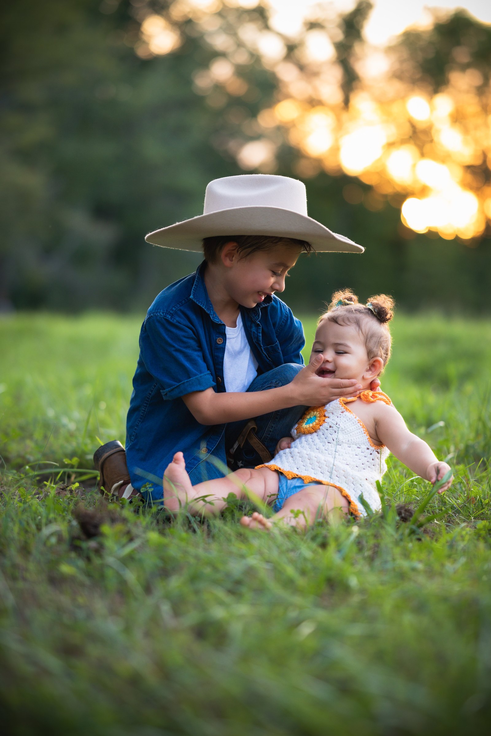 Older brother smiling with his baby sister in a sunlit field