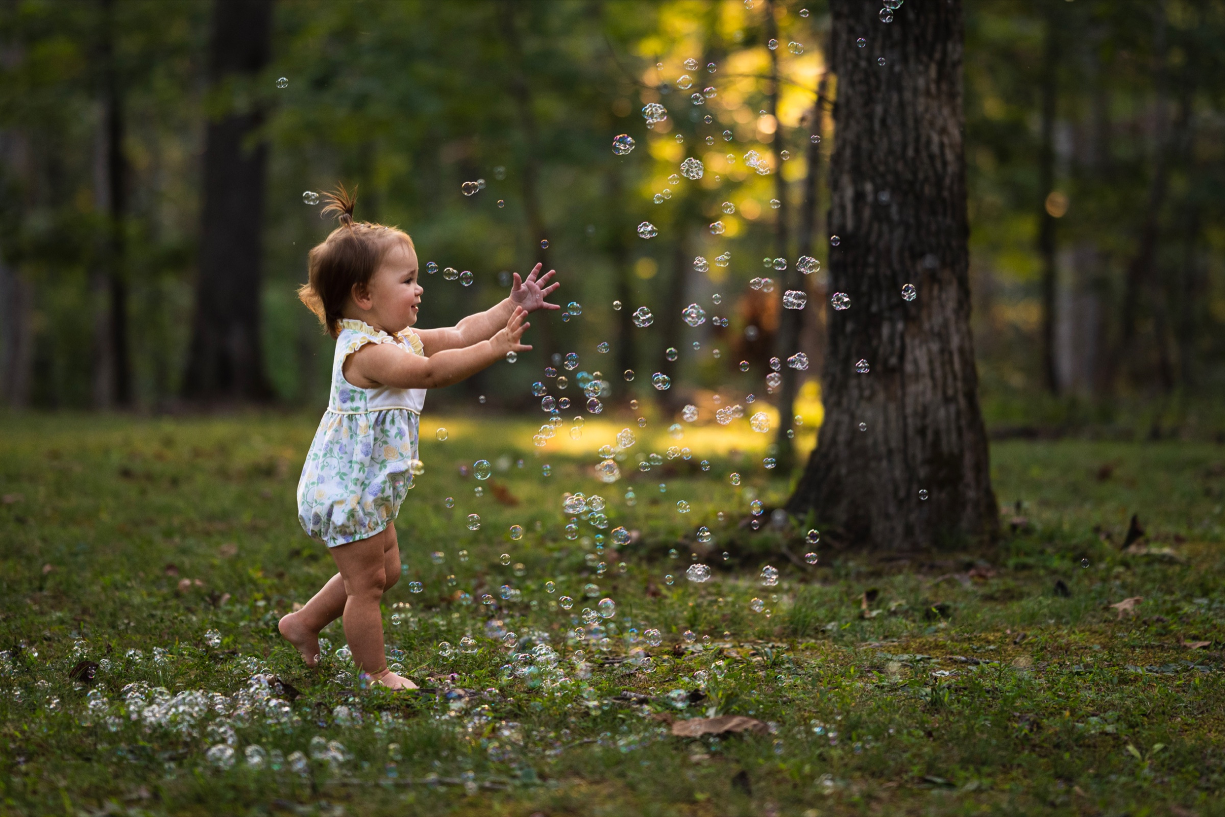 Young child reaching toward bubbles in a sunlit woodland