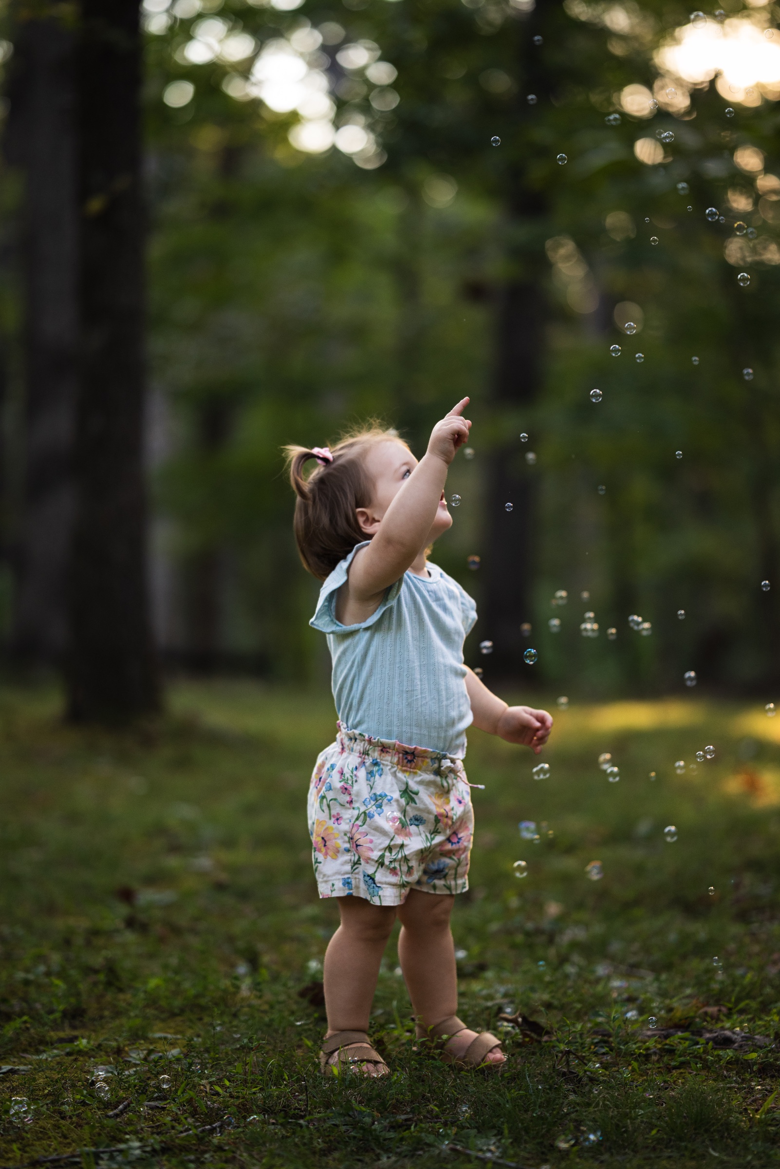Young child pointing toward bubbles in a wooded clearing