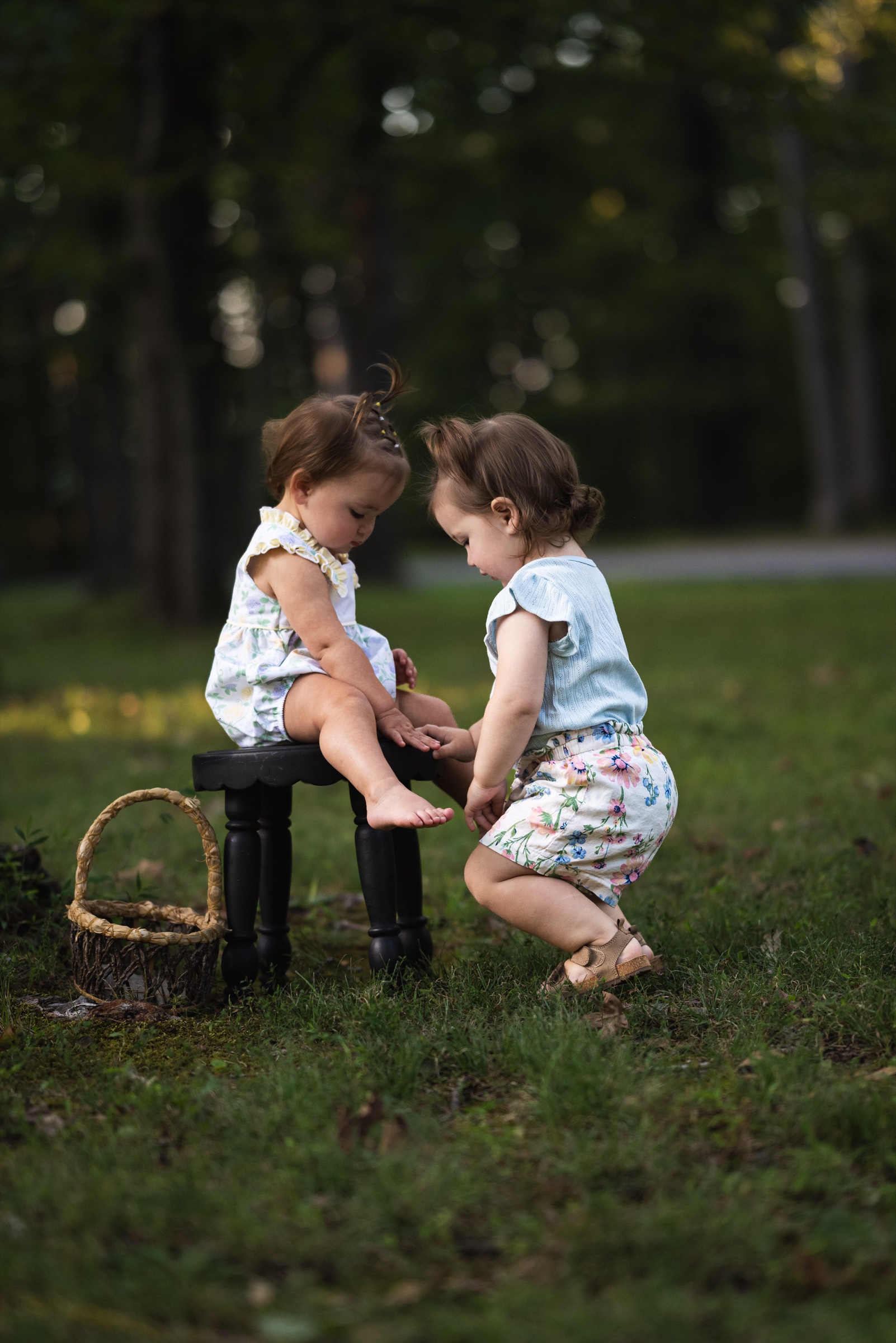 Two young children sharing a quiet moment beside a stool in a wooded clearing